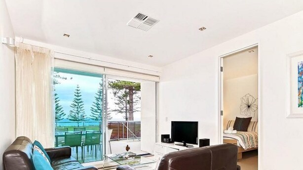 A modern living room with a large sliding glass door leading to a balcony, a flat-screen TV, and a comfortable seating area. - Breeze Beachfront Apartments (Victor Harbor)