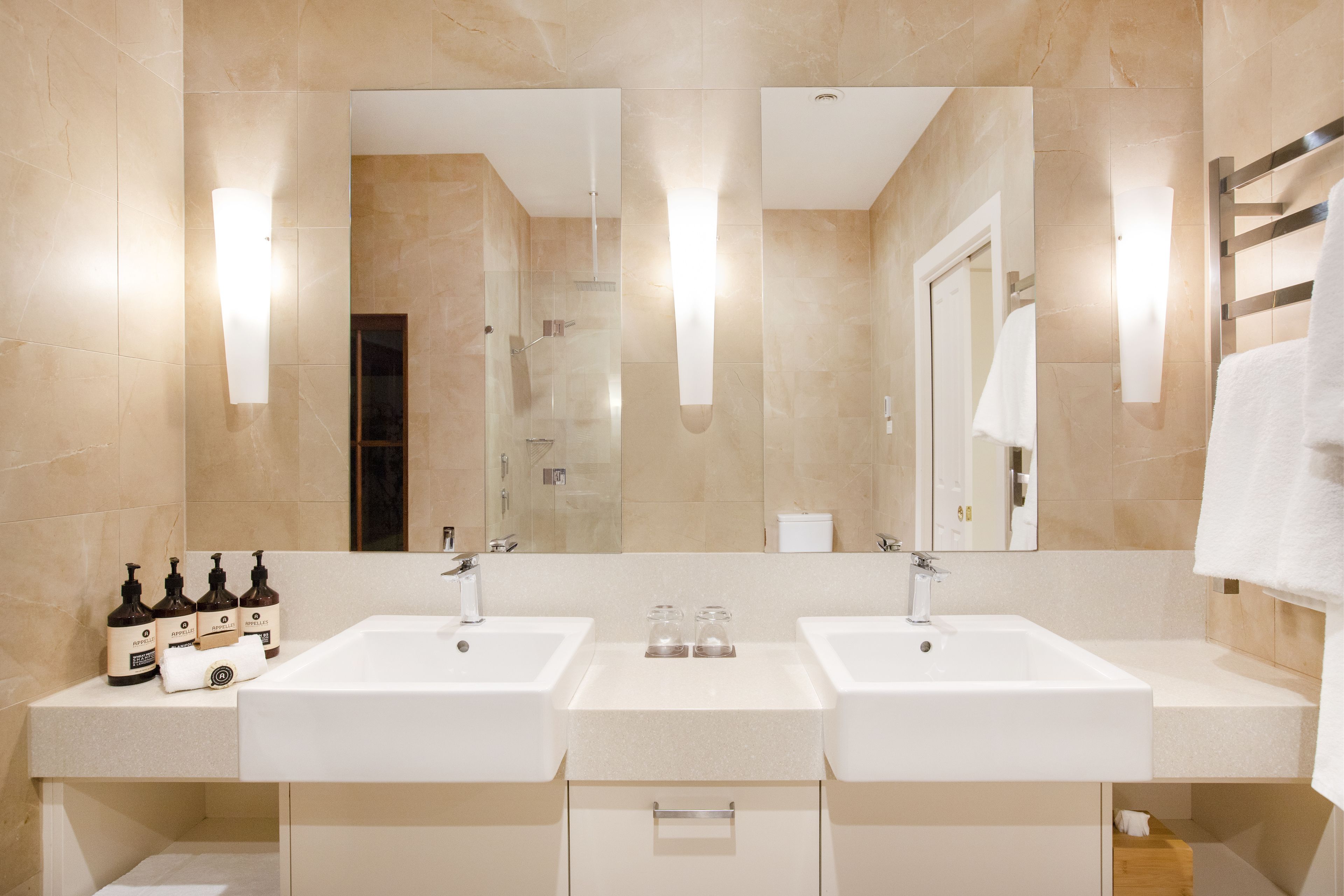 Un bagno moderno con due lavabi, uno specchio grande e un portasciugamani.