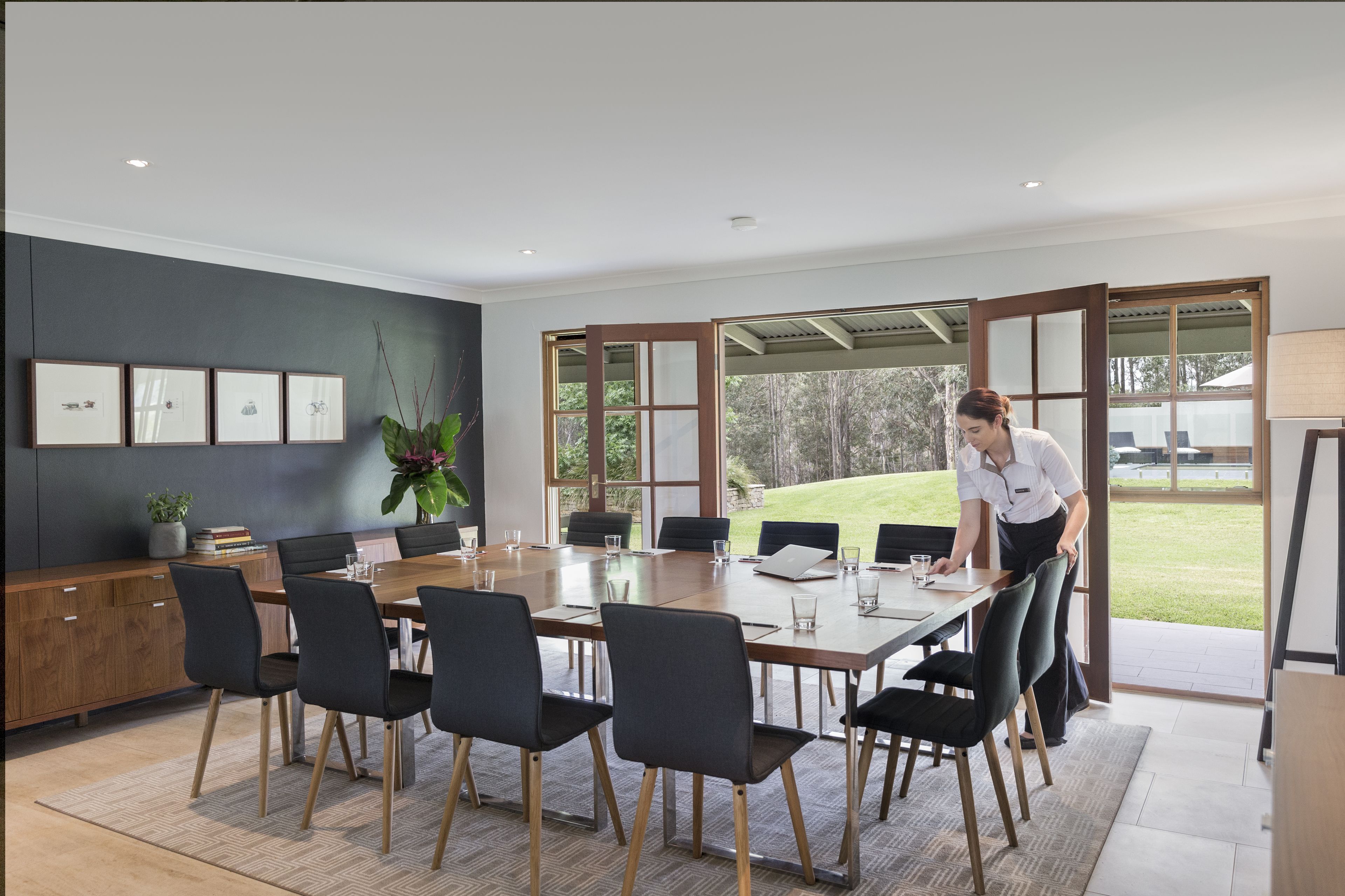Un comedor moderno con una gran mesa de madera, sillas negras y vistas a un área exterior con césped a través de amplios ventanales.
