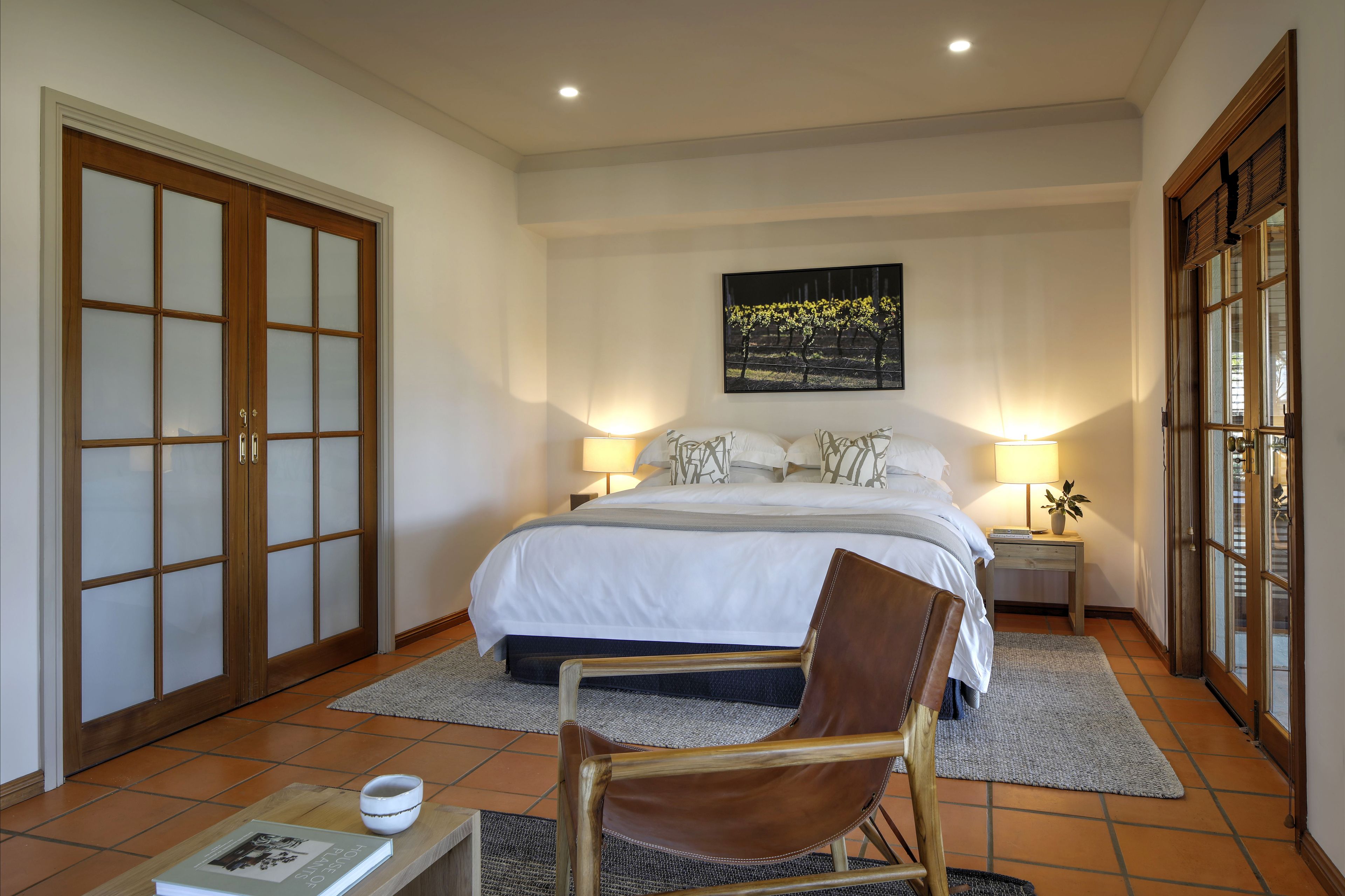 A bedroom with a large bed, two bedside tables with lamps, a chair, a rug, and a sliding glass door.