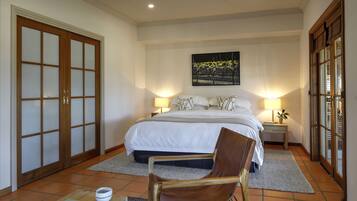 A bedroom with a large bed, two bedside tables with lamps, a chair, a rug, and a sliding glass door.