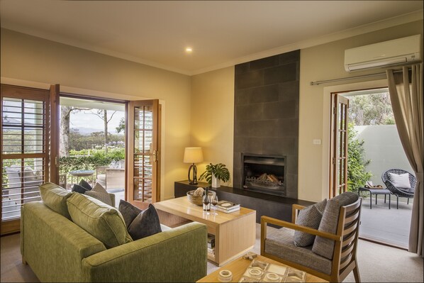 A living room with a sofa, armchair, and a coffee table. There is a fireplace and a view of the outdoors through large windows. - Spicers Vineyards Estate (Pokolbin)