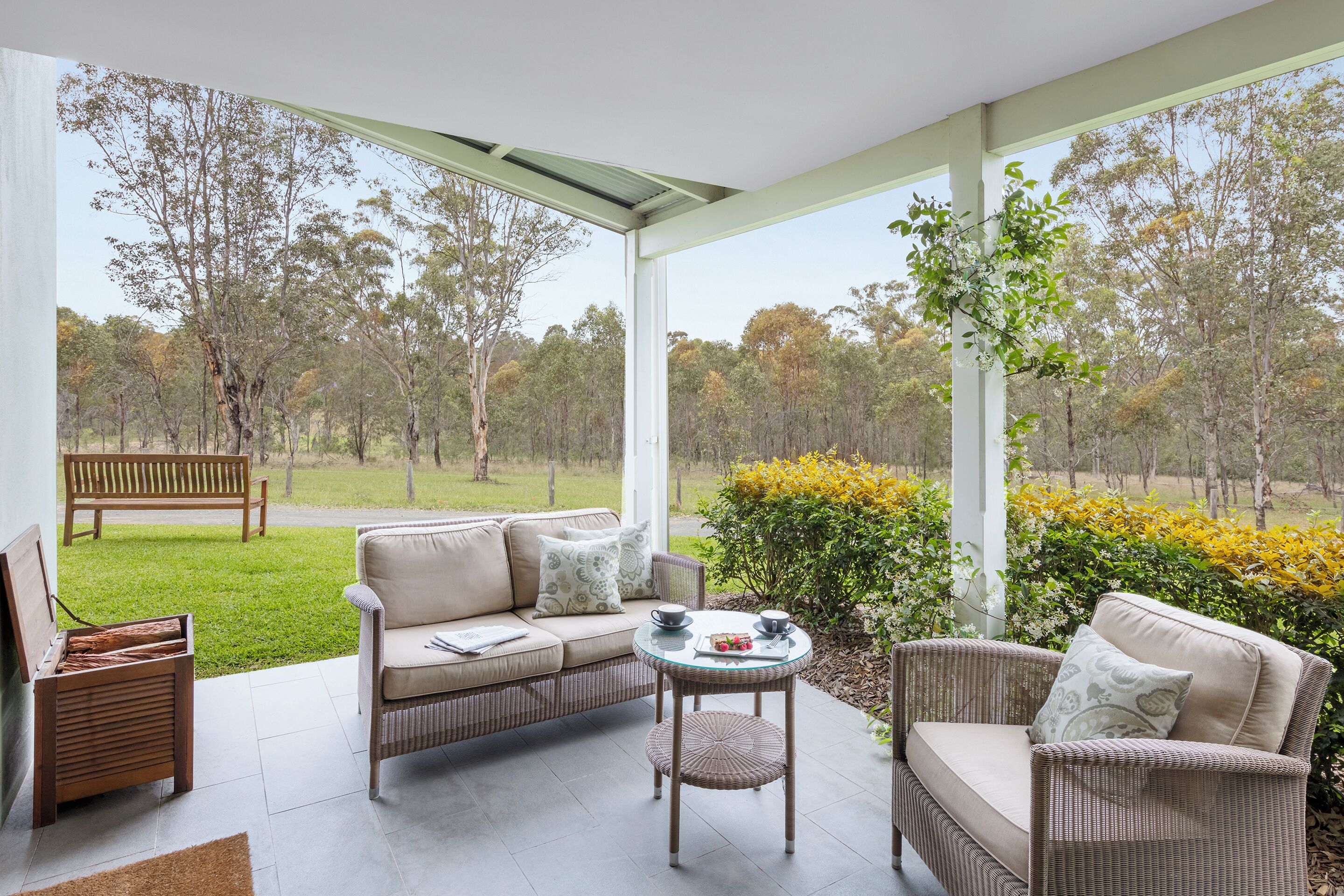 A modern outdoor seating area with a sofa, chairs, and a small table, overlooking a grassy field and trees.