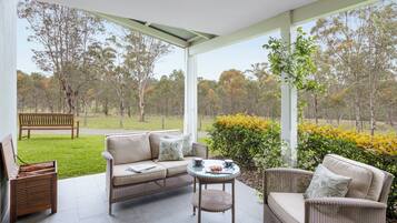 A modern outdoor seating area with a sofa, chairs, and a small table, overlooking a grassy field and trees.