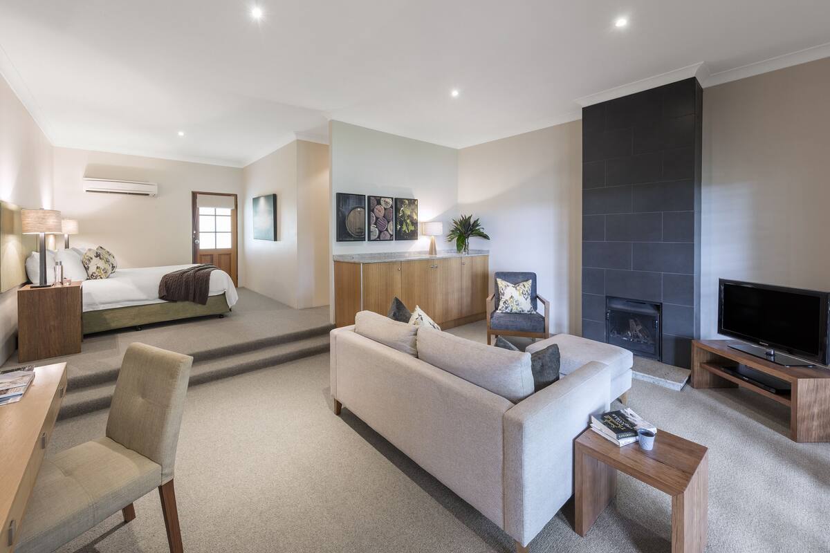 A modern living room with a sofa, coffee table, TV, fireplace, and a bed in the background.