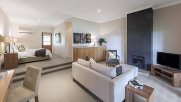 A modern living room with a sofa, coffee table, TV, fireplace, and a bed in the background.