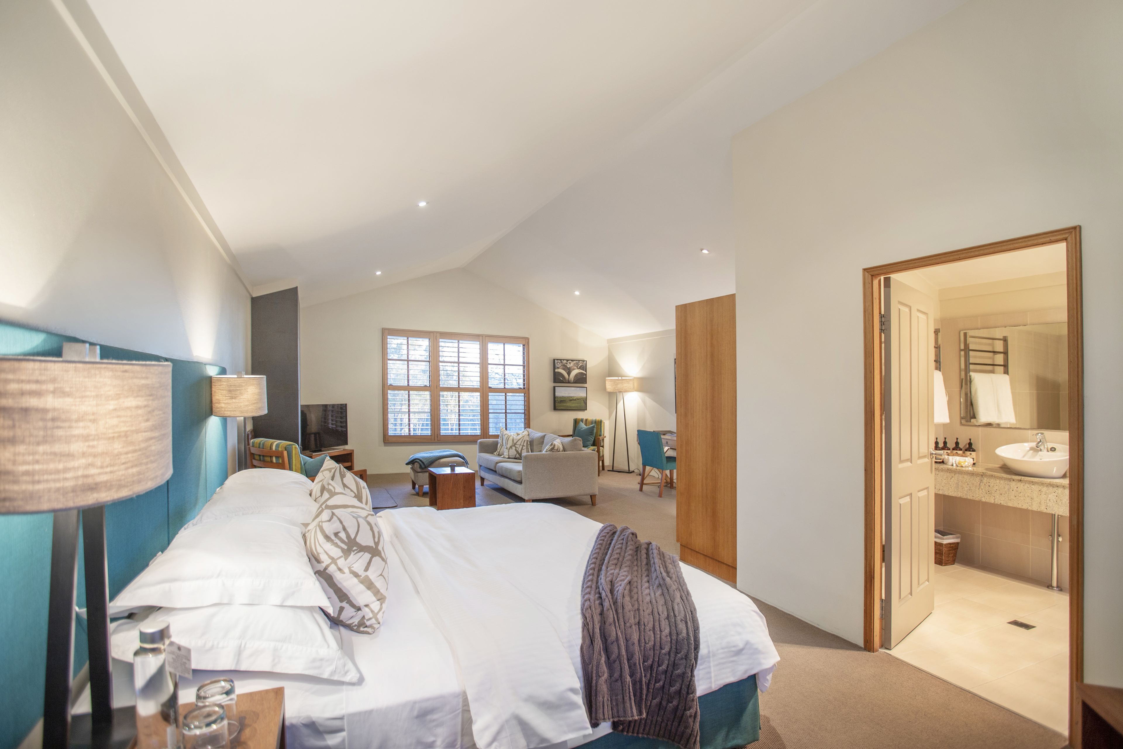 A spacious bedroom with a large bed, bedside tables, a desk, and a view of the bathroom.