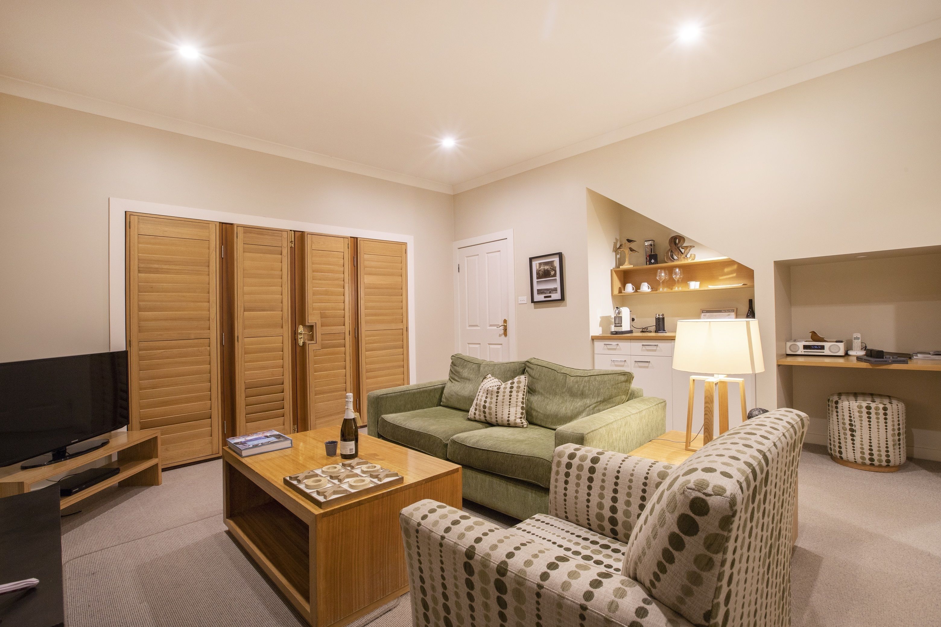 A living room with a television, wooden wardrobe, green sofa, patterned armchairs, a coffee table, and a lamp.