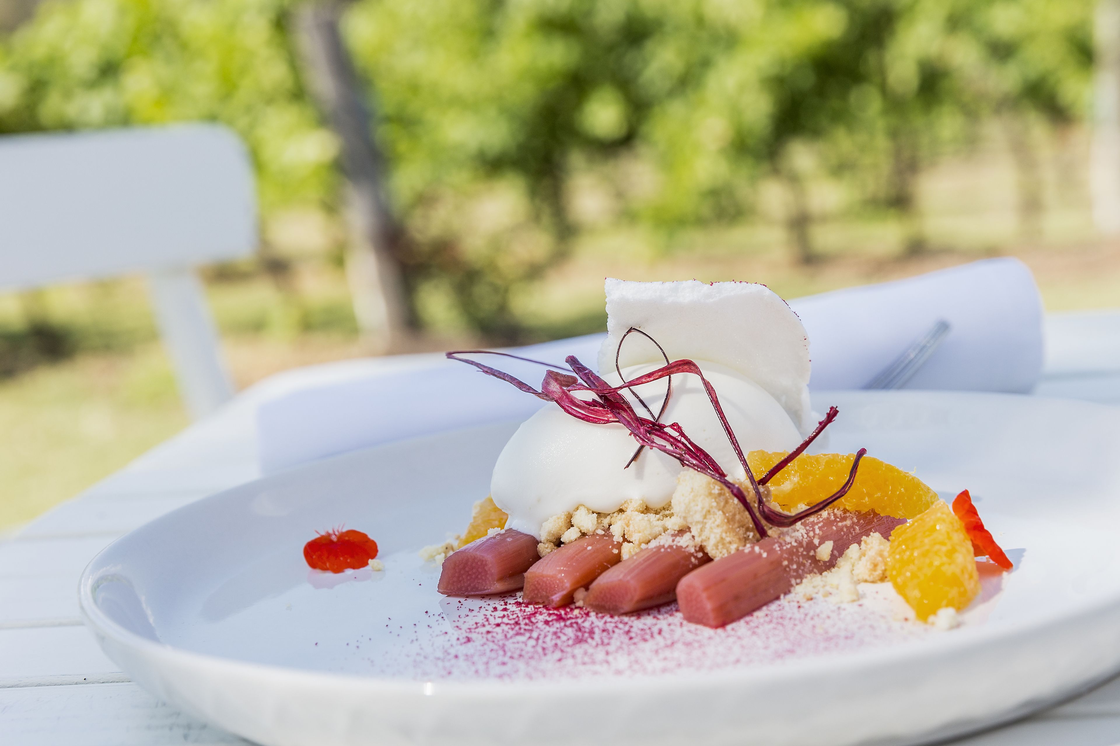 Postre en un plat blanc amb una tovallola blanca, decorat amb fruita vermella i groga, i una bola blanca a dalt.