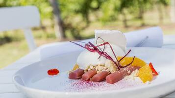 Postre en un plat blanc amb una tovallola blanca, decorat amb fruita vermella i groga, i una bola blanca a dalt.