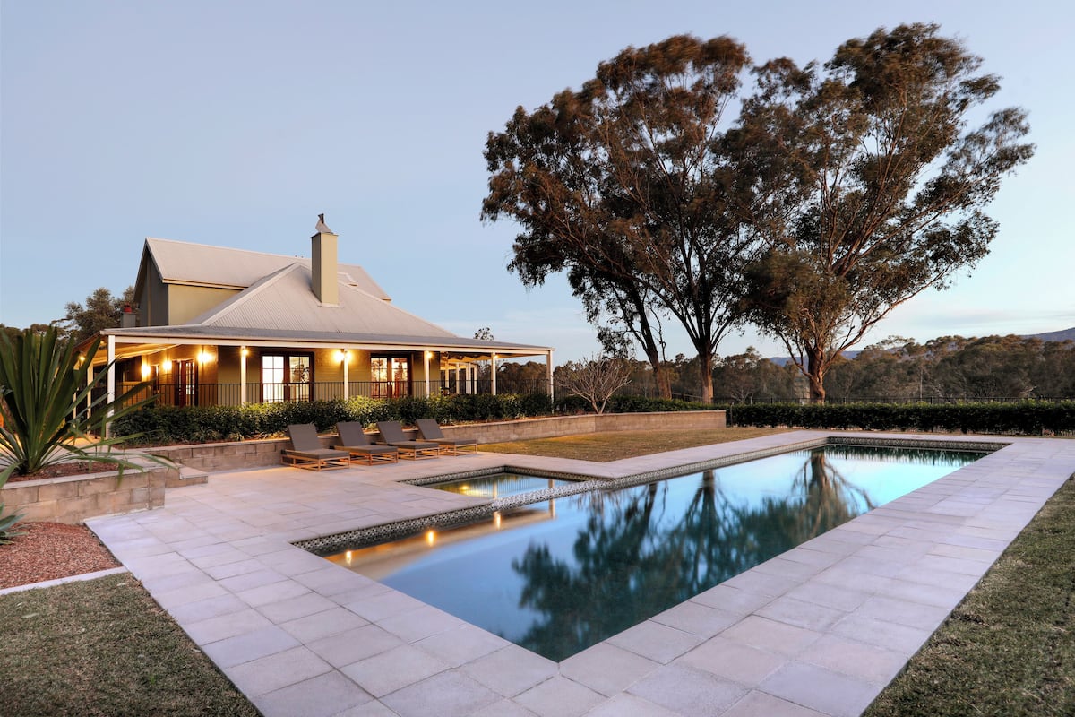 A house with a swimming pool, outdoor seating, and a large tree.