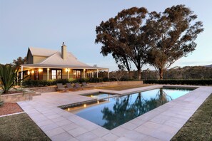 Una casa con piscina, mobiliario exterior y un gran árbol.