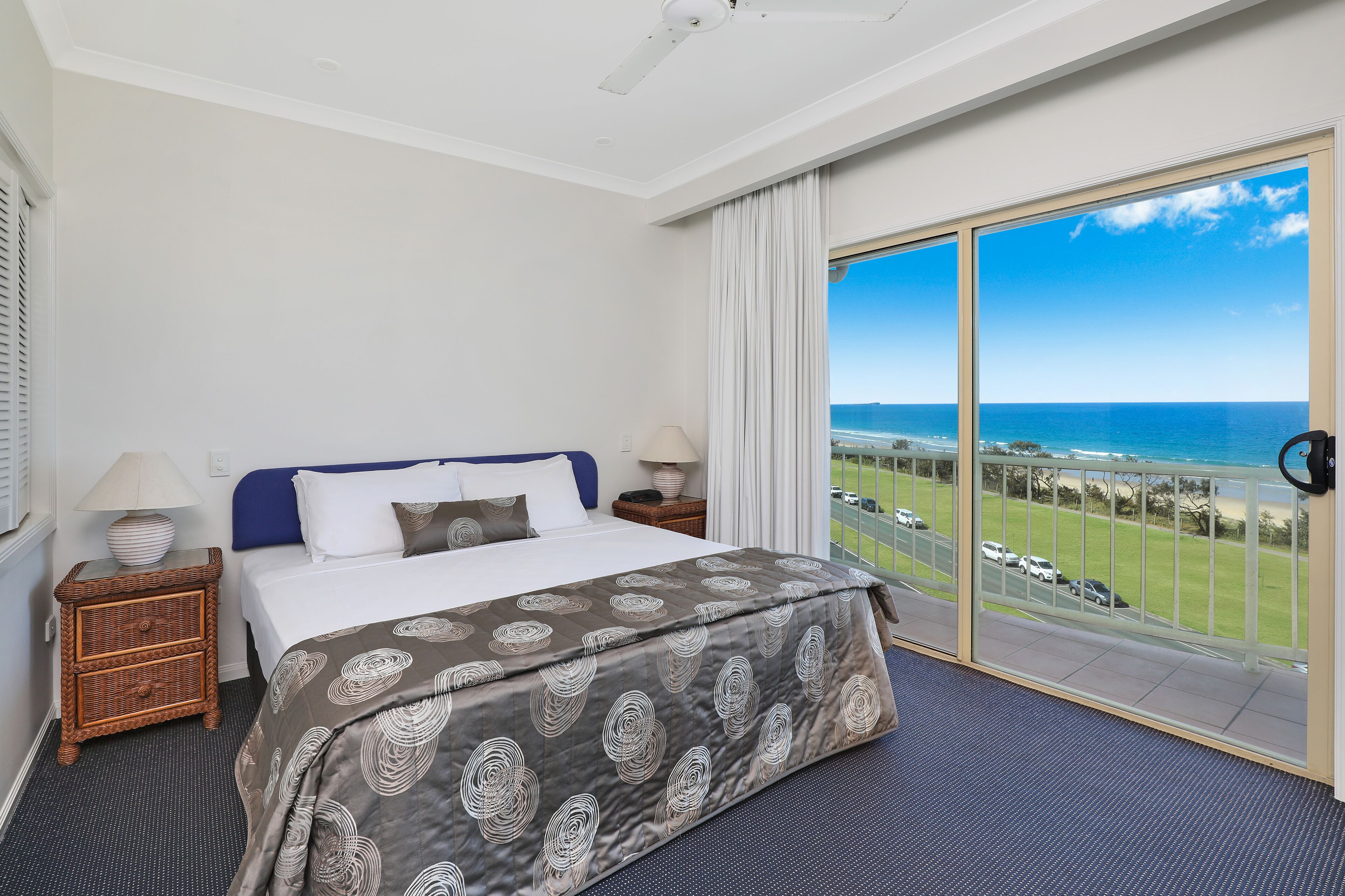Ein Hotelzimmer mit Bett, Nachttisch, Lampe und Blick auf das Meer.