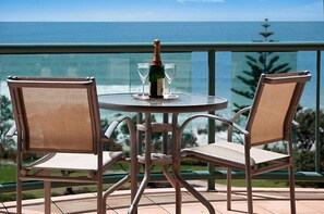 Ett runt bord med två stolar, en flaska champagne och två glas på en balkong med utsikt över havet.