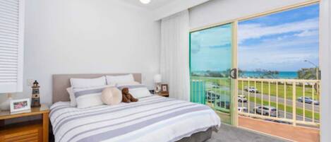 Une chambre avec un grand lit, une table de chevet, une lampe et une vue sur l’extérieur grâce à un balcon.