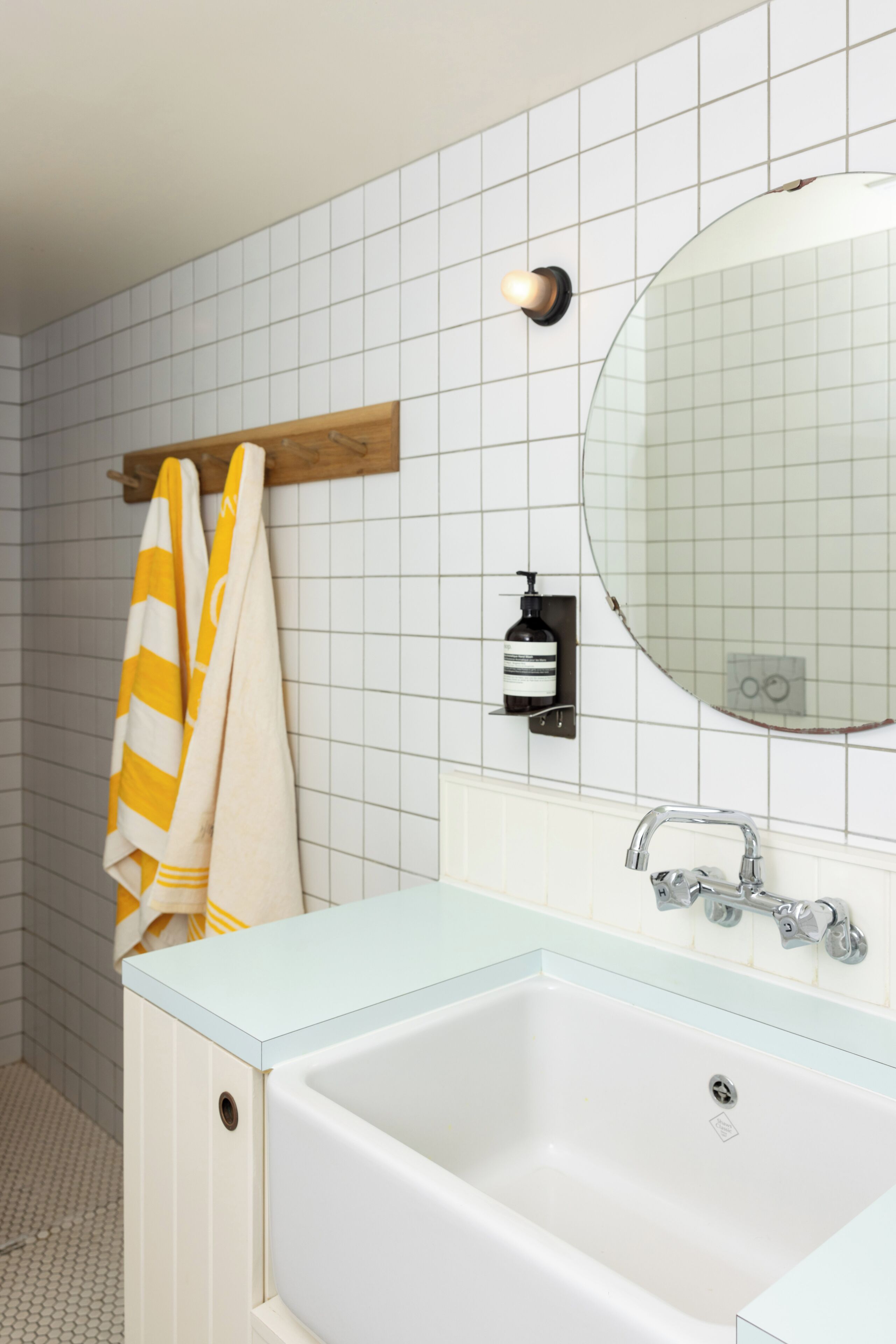 Een badkamer met een wit bad, een houten handdoekhouder, een ronde spiegel en een zeepdispenser aan de muur.