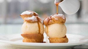 Two ice cream sundaes with caramel sauce being poured over them.