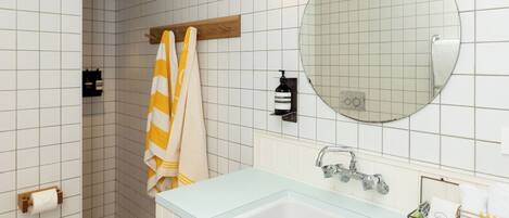 Ein modernes Badezimmer mit einer großen Badewanne, einer Dusche und einem WC. Ein Handtuchhalter mit einem gestreiften Handtuch und ein runder Spiegel über dem Waschbecken.