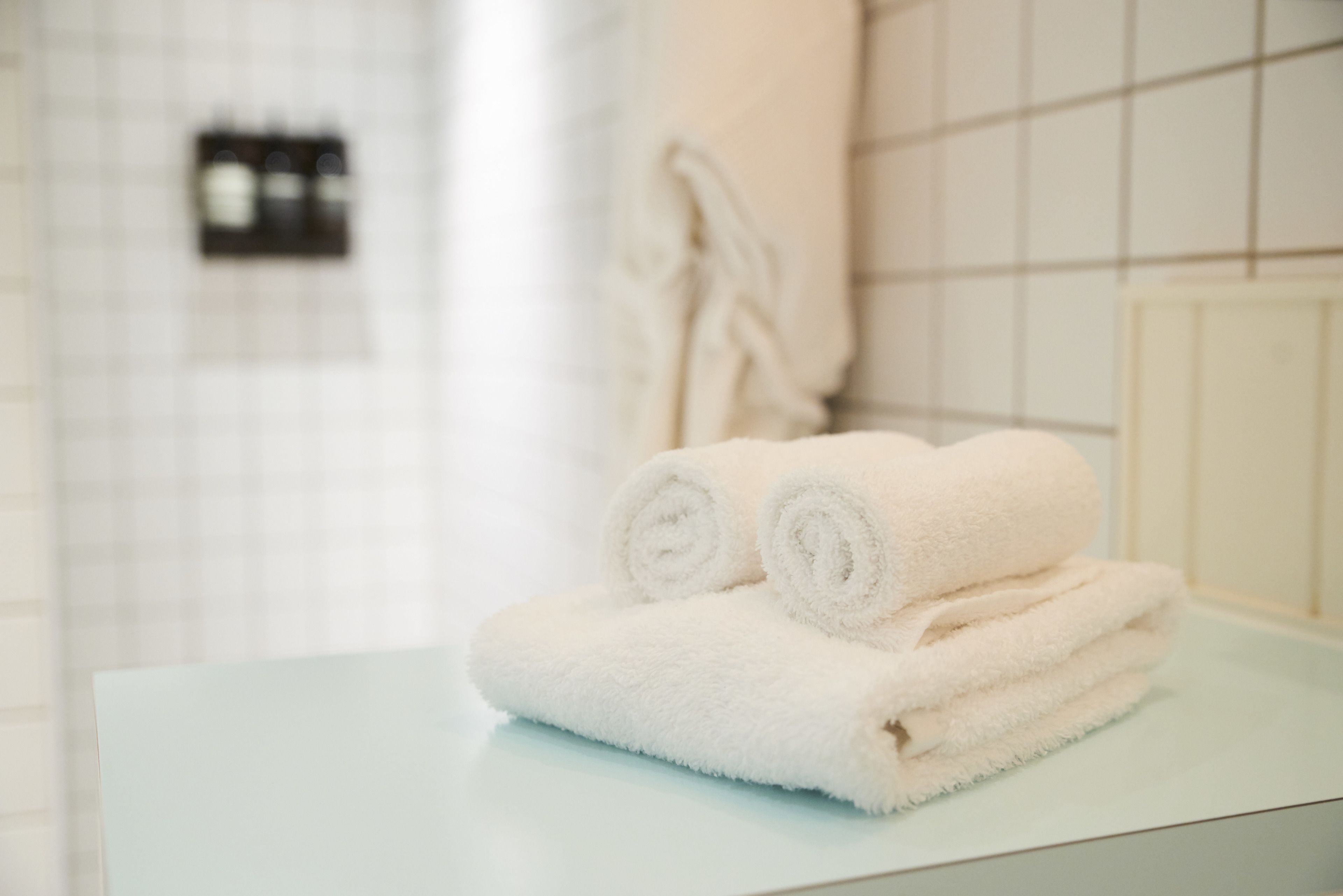 Un montón de toallas blancas sobre una encimera azul claro en un baño con baldosas blancas.