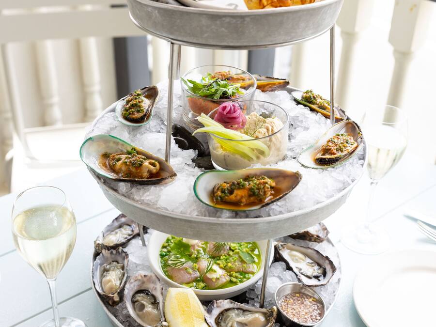 A multi-tiered seafood platter with oysters, bread, and a glass of white wine on a table.