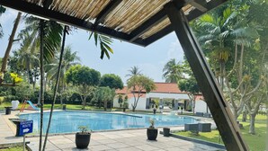 A swimming pool with a clear evacuation route sign, surrounded by palm trees and a building with a red-tiled roof. - Grand Elty Krakatoa (Kalianda)