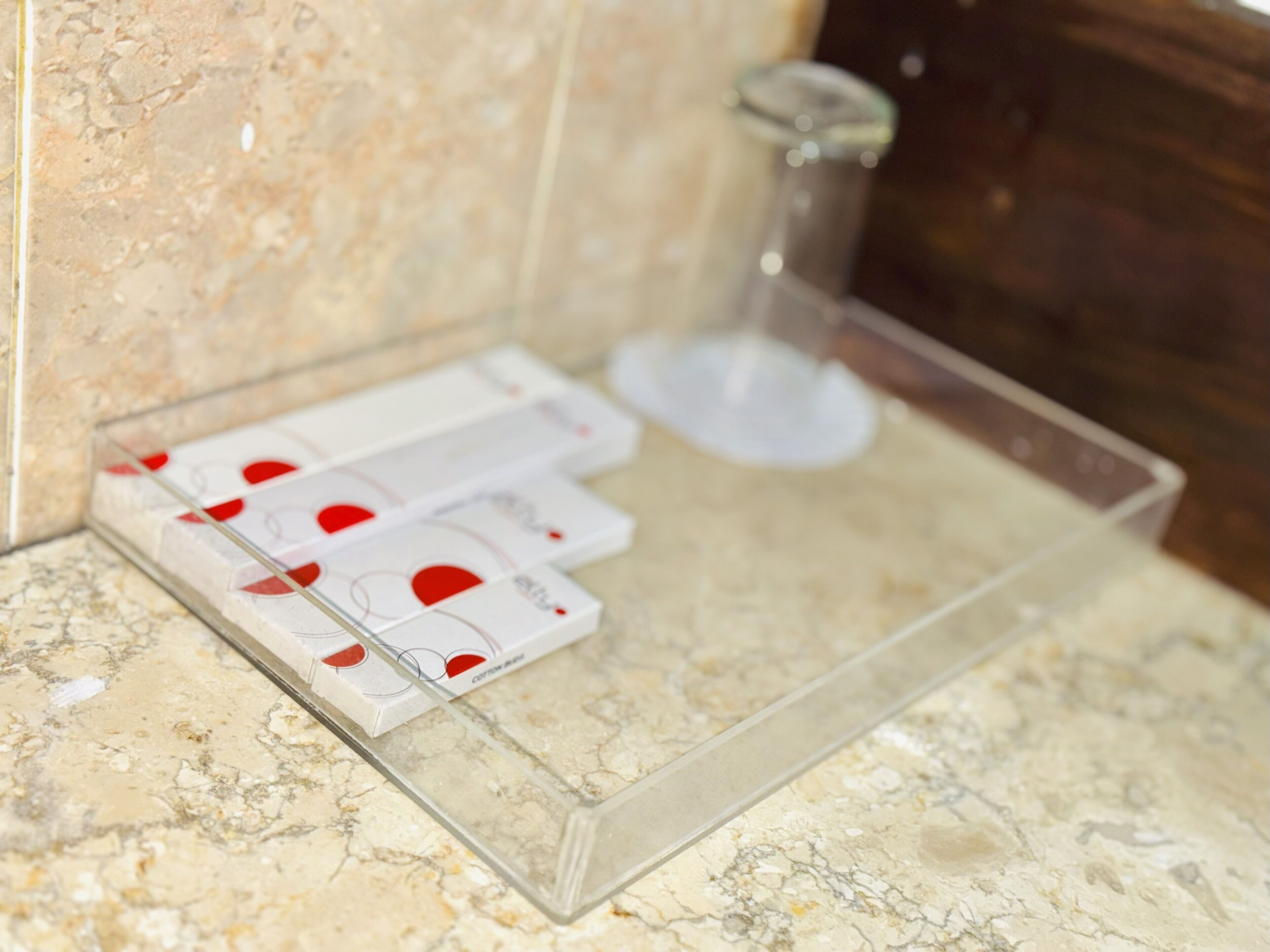 A bathroom with a marble countertop, a glass soap dish, and a shower area.
