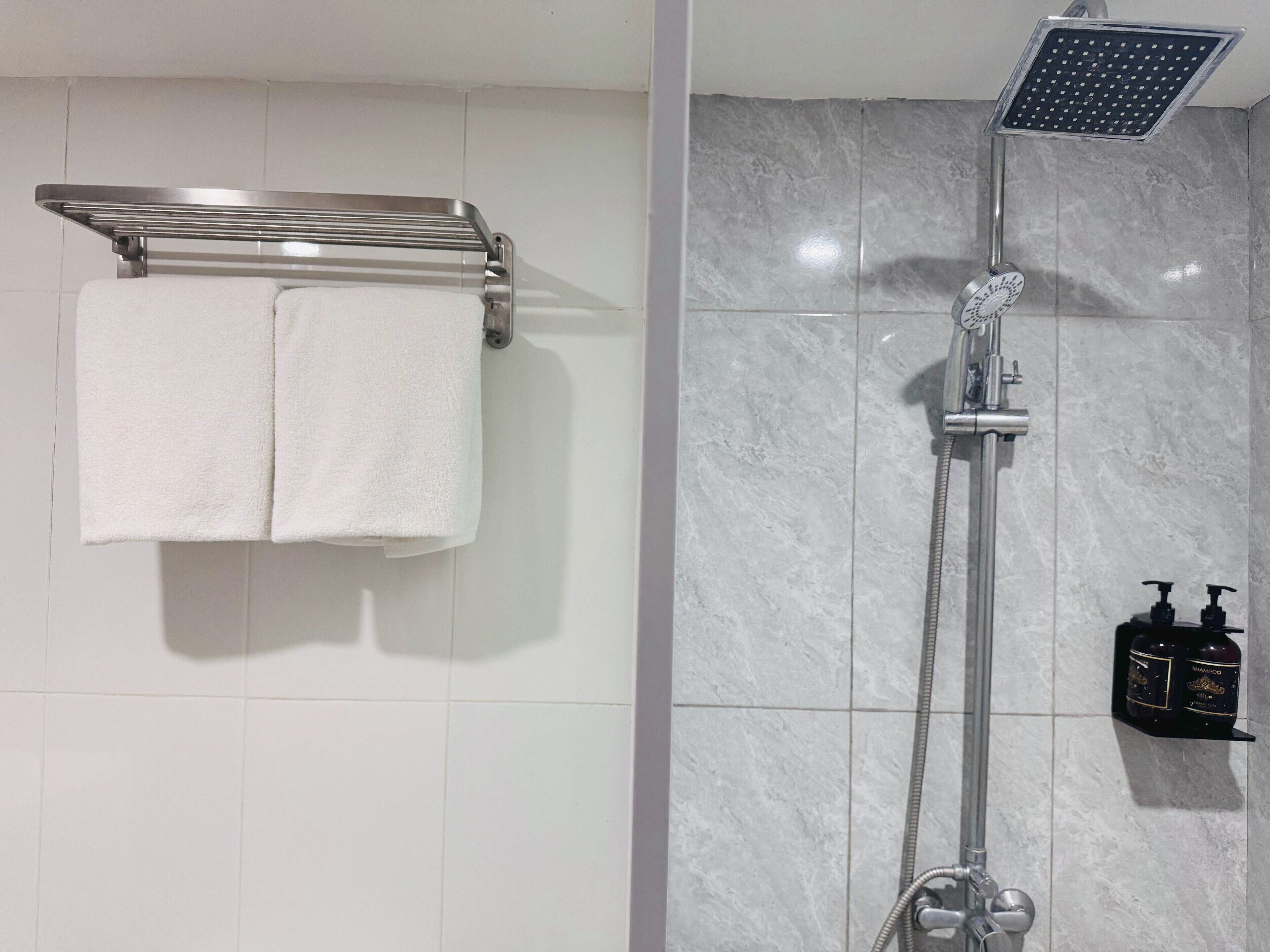 A bathroom with a shower, a towel rack with two towels, and a shelf with two bottles.
