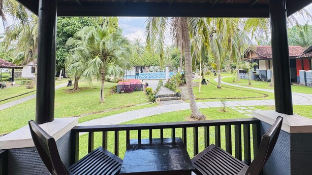 A covered outdoor seating area with a view of a pool and palm trees. - Grand Elty Krakatoa (Kalianda)
