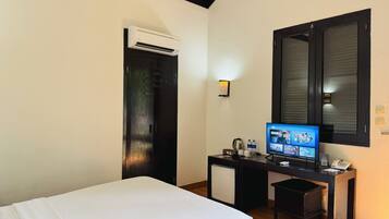 A hotel room with a bed, desk, and air conditioning unit.