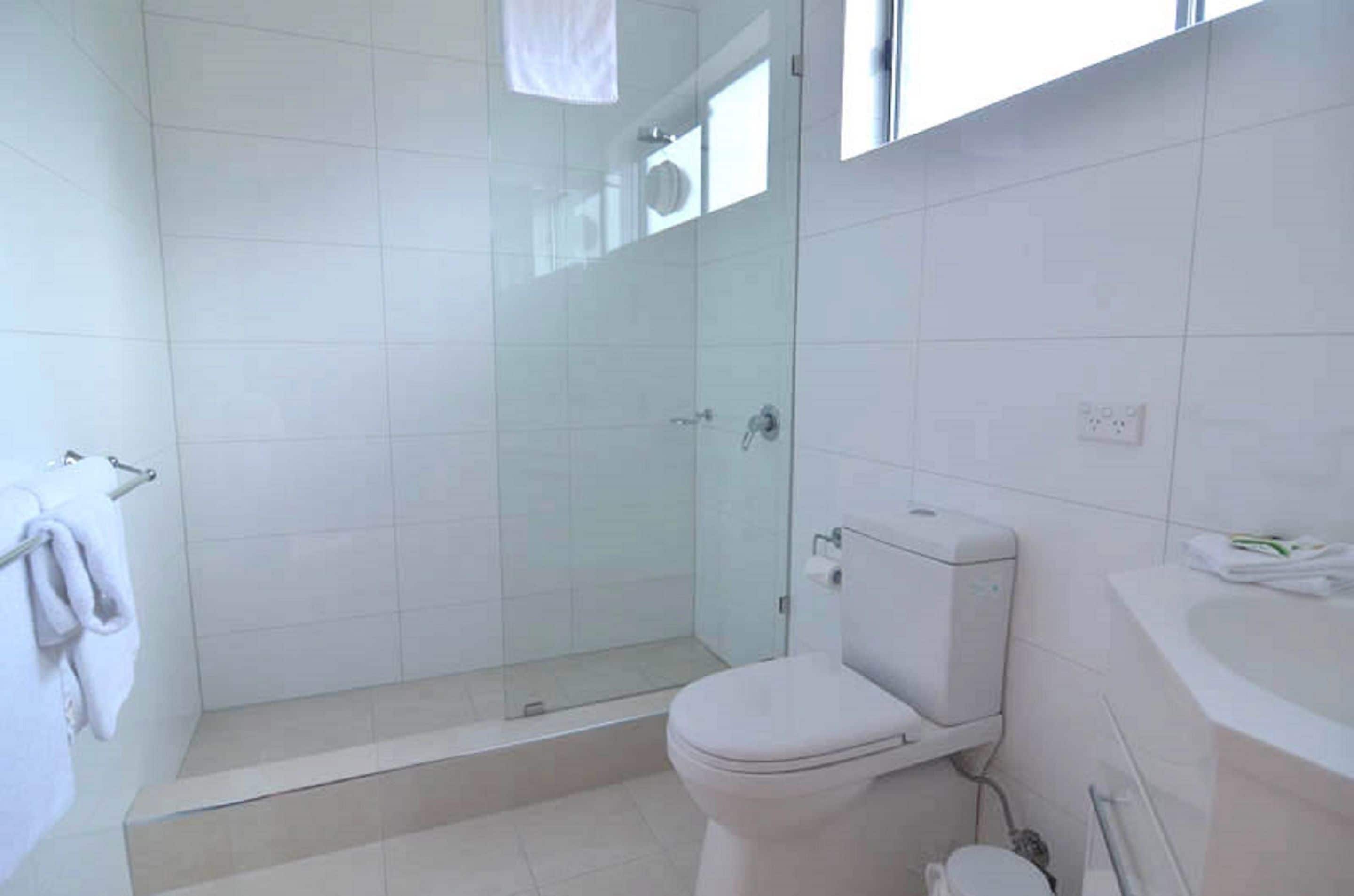 A bathroom with a glass-enclosed shower, a toilet, and a sink.