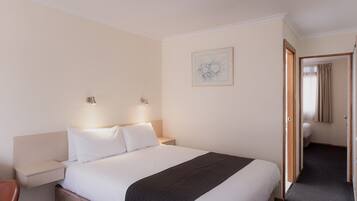 Habitación de hotel con una cama grande, mesitas de noche, un buró, un cuadro en la pared y una puerta que da a otra habitación.