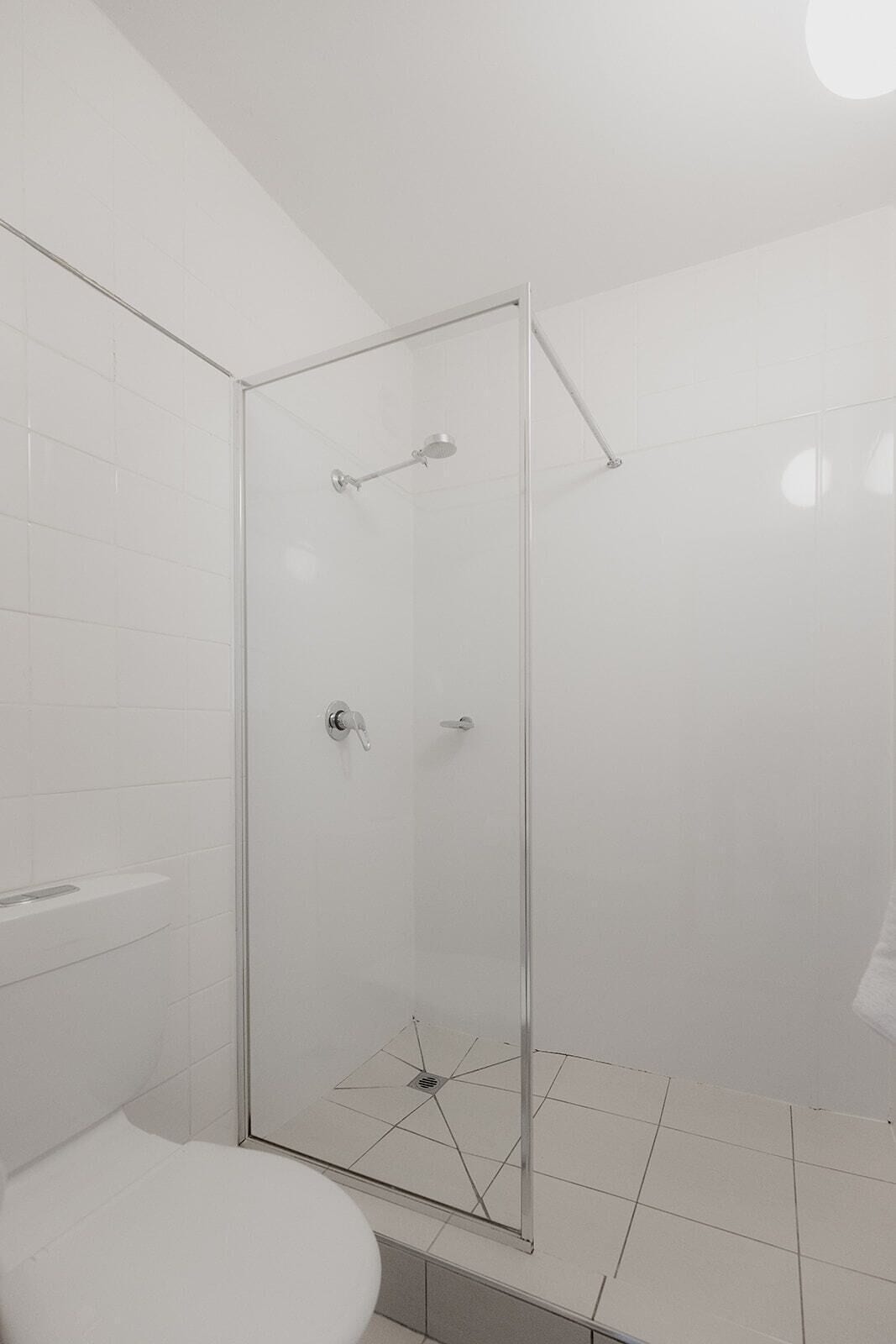 Un baño moderno con cabina de ducha de vidrio, paredes con azulejos blancos y un inodoro blanco.