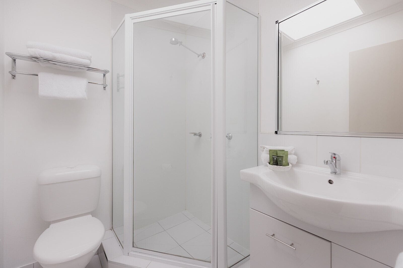 A modern bathroom with a glass-enclosed shower, a white toilet, a sink with toiletries, and a mirror.