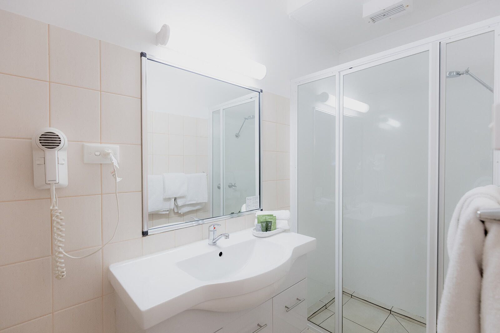 A modern bathroom with a white sink, a hairdryer, a mirror, and a glass shower enclosure.