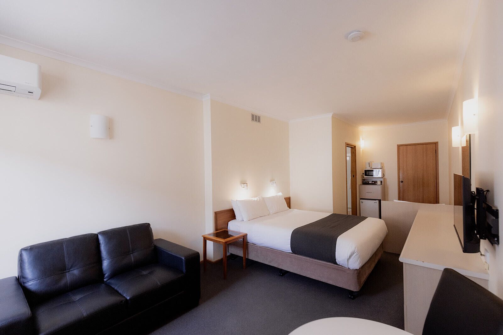 A hotel room with a bed, a sofa, a small table, a TV, and a microwave.