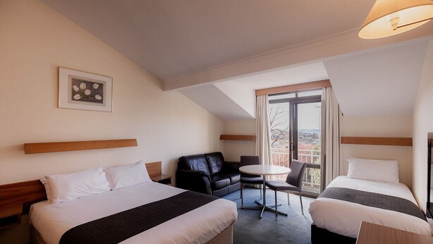 Une chambre d’hôtel avec deux lits, un bureau, une chaise et une grande fenêtre donnant sur un beau paysage.