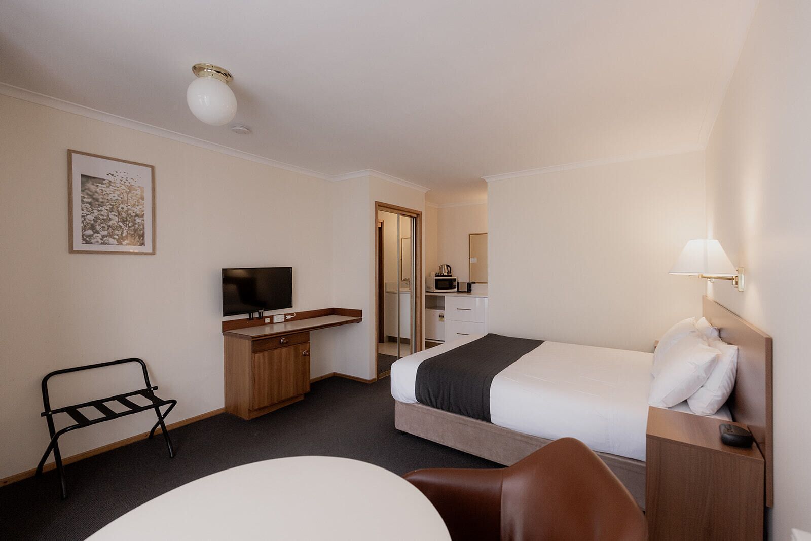 A hotel room with a bed, a desk, a chair, a television, and a microwave.