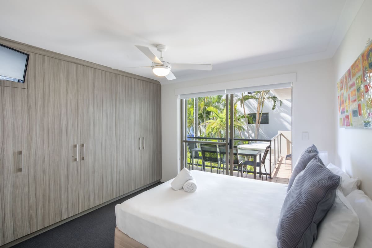 Quarto de hotel com cama, ventilador de teto, televisão e varanda com área de estar externa.