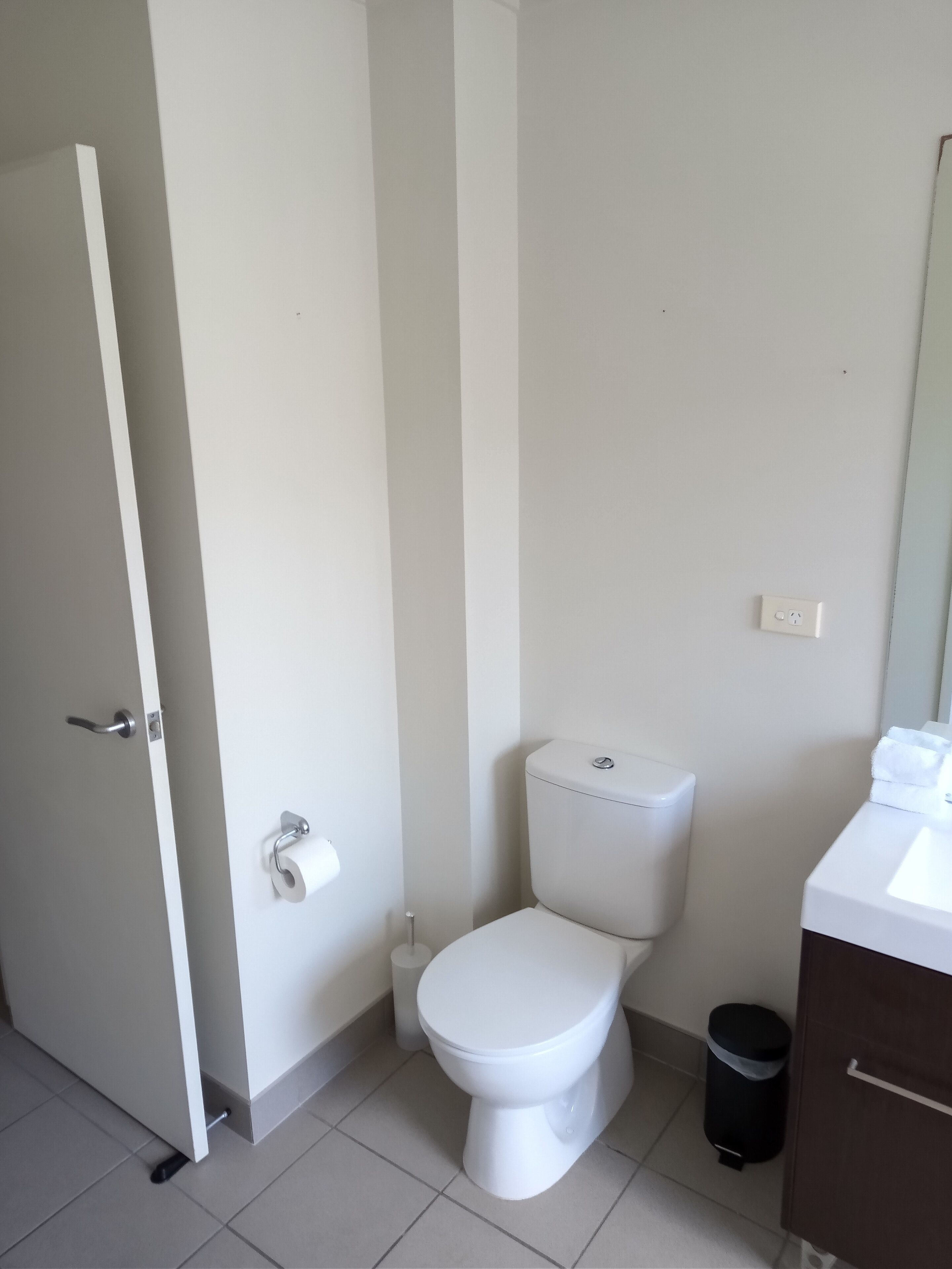 A bathroom with a toilet, a sink, a trash bin, and a door.