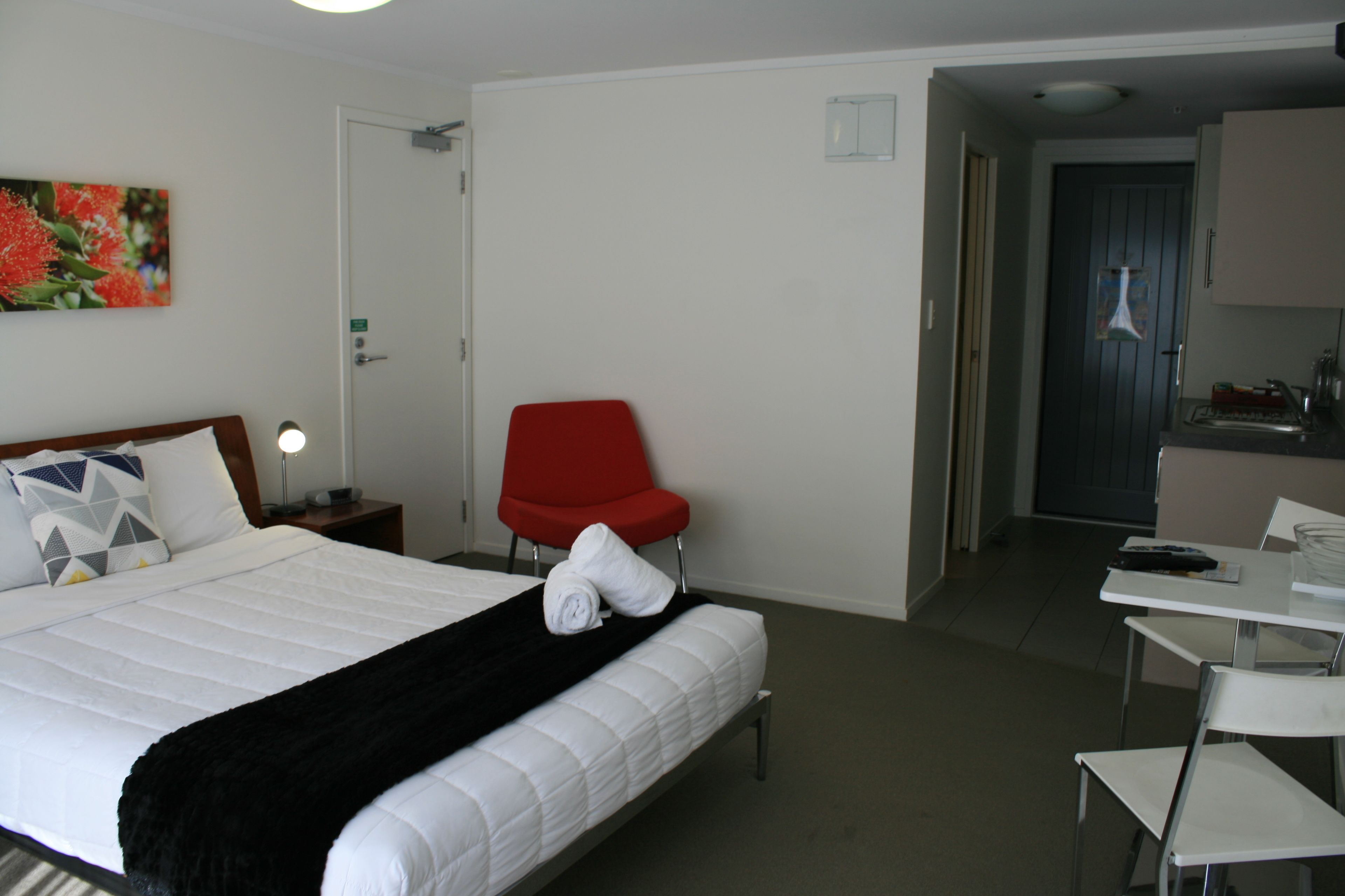 A hotel room with a bed, a red chair, a desk, and a kitchenette.