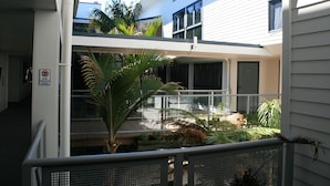 A multi-level building with a balcony area featuring potted plants and a view of the surrounding area. - Atlas Suites And Apartments (Tauranga)