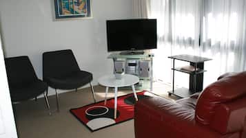 Una sala de estar moderna con un televisor de pantalla plana, dos sillas negras, un sofá de cuero rojo y una mesa de centro de vidrio.