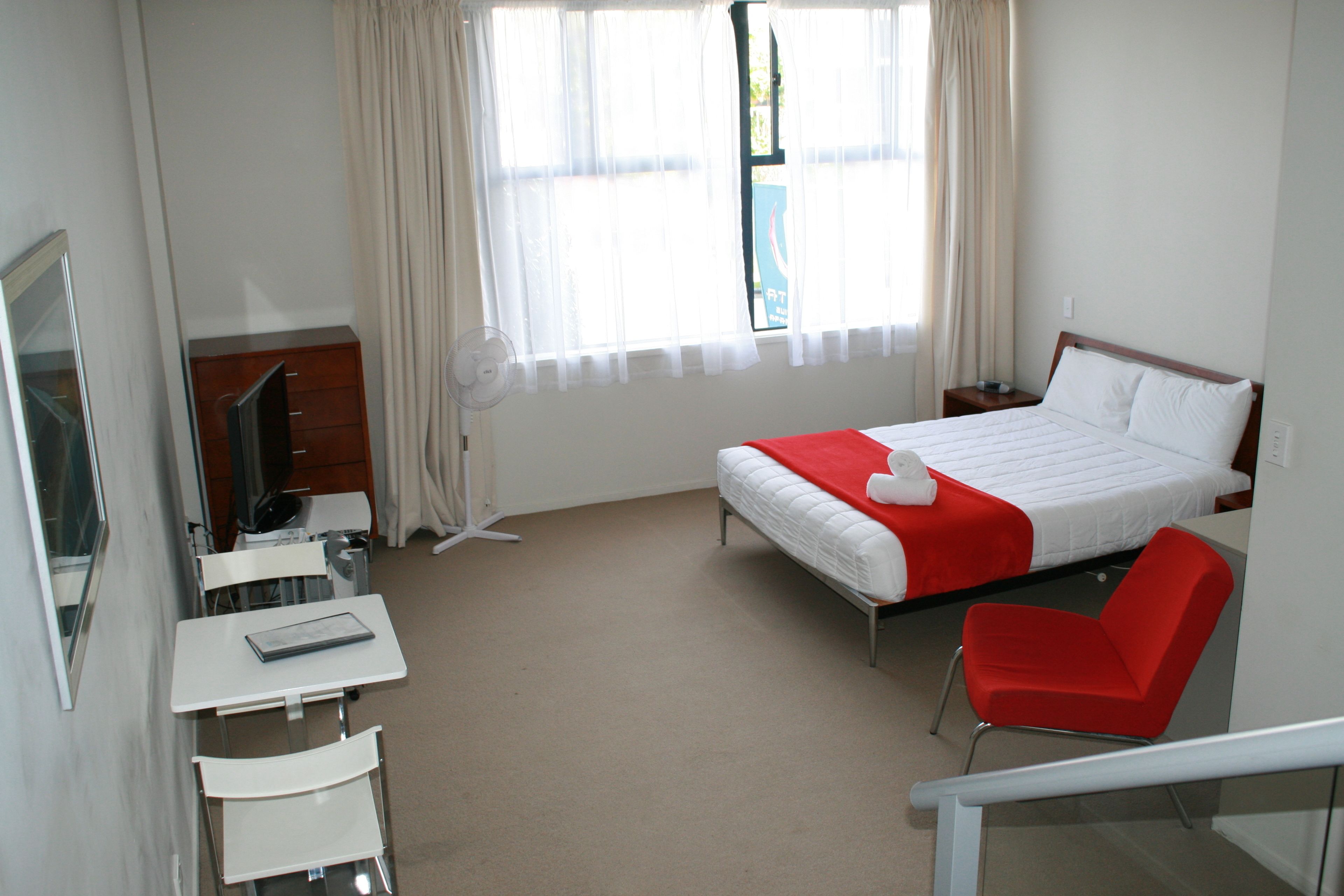 Una habitación de hotel con cama, escritorio con silla, televisión y ventana con cortinas.