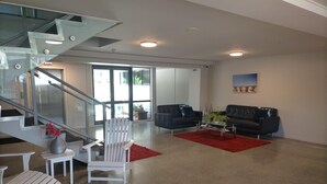 A spacious living area with a modern staircase, two sofas, a red rug, and a white chair. - Atlas Suites And Apartments (Tauranga)