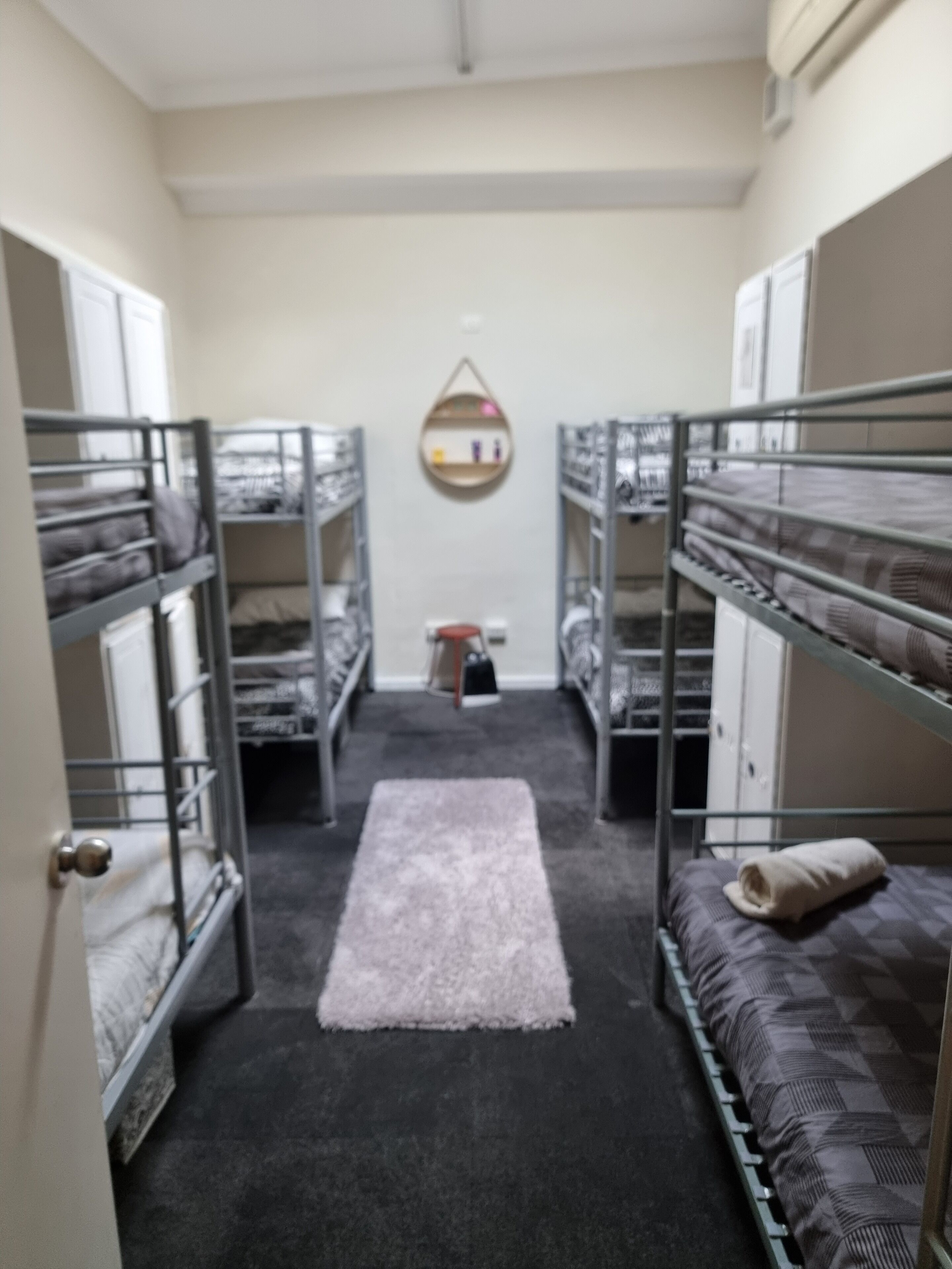 A narrow corridor with bunk beds on either side, a small rug on the floor, and a wall-mounted shelf with items.