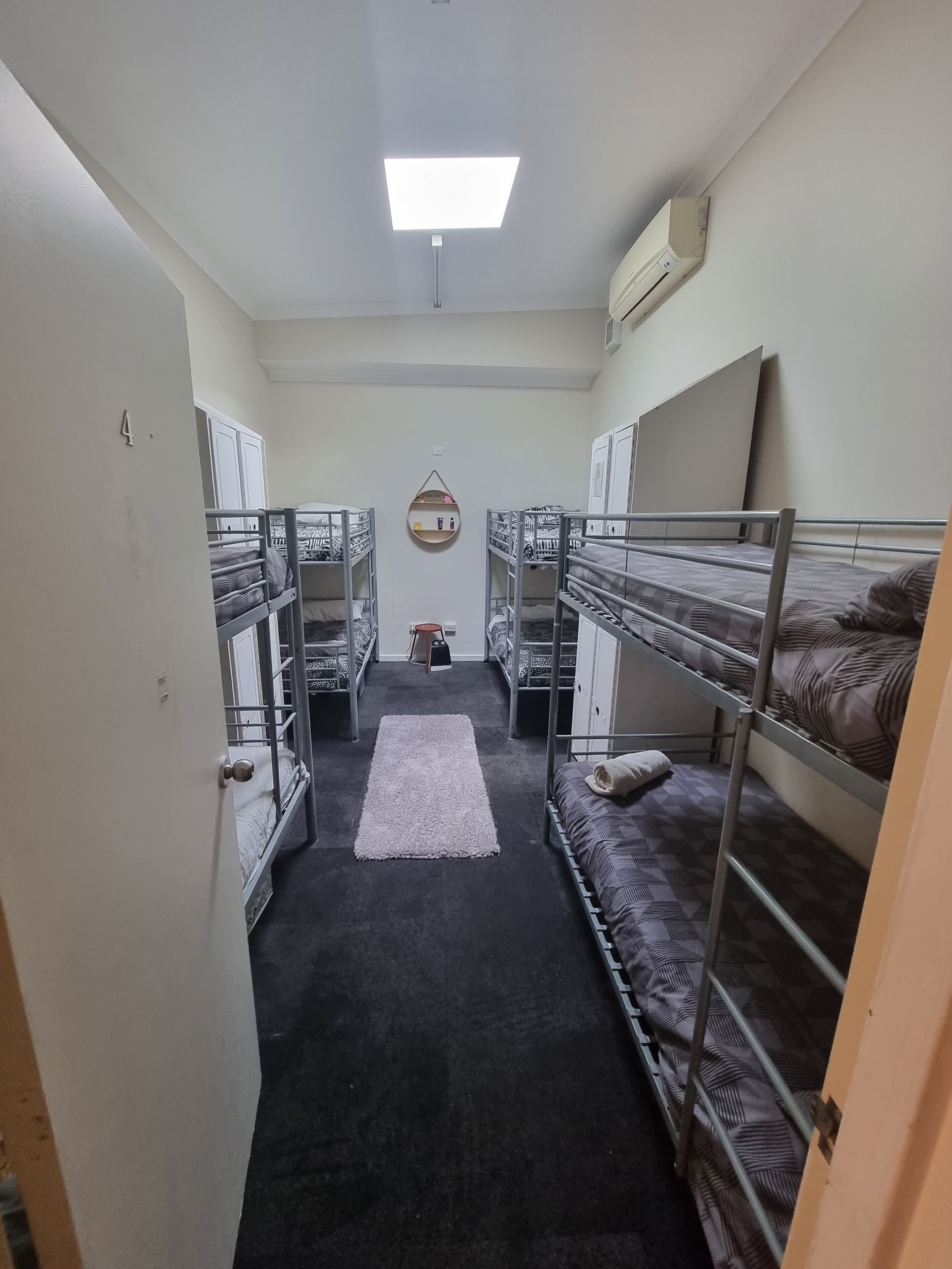 A narrow corridor with bunk beds on either side, a central rug, and a ceiling light.