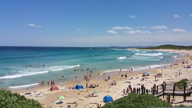 A beach with people swimming and sunbathing, a wooden pier, and a clear blue sky. - The Entrance Backpackers - Hostel (The Entrance)