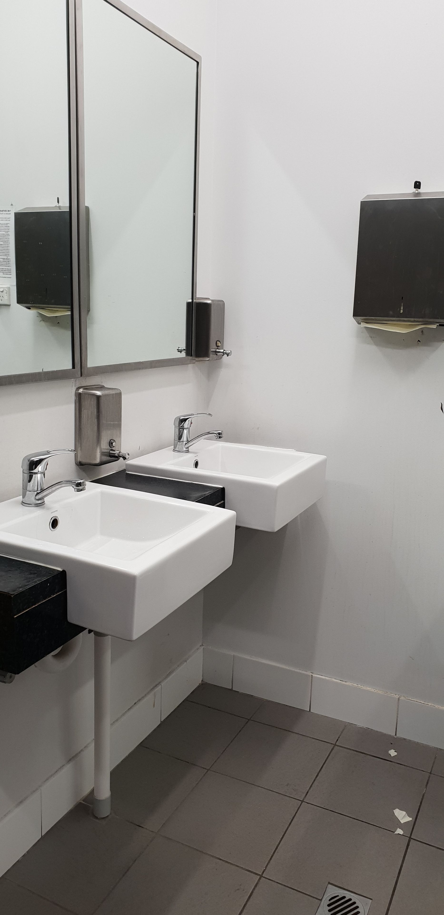 A restroom with two sinks, a mirror, and a soap dispenser.
