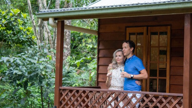 A wooden cabin with a lattice balcony, surrounded by dense greenery. - Sunshine Valley Cottages (West Woombye)