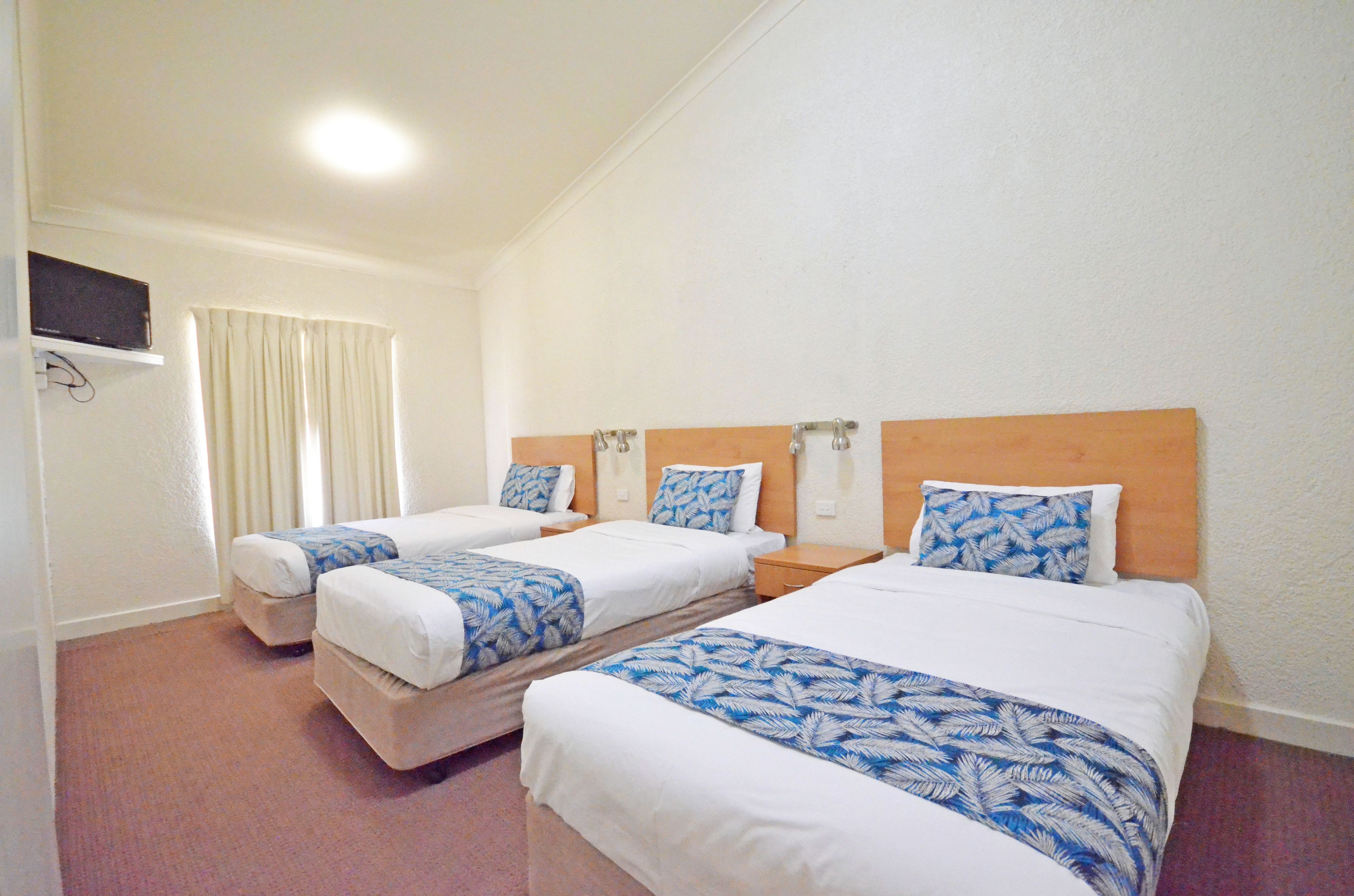 A hotel room with two single beds, each with a wooden headboard and a blue leaf-patterned bedspread.